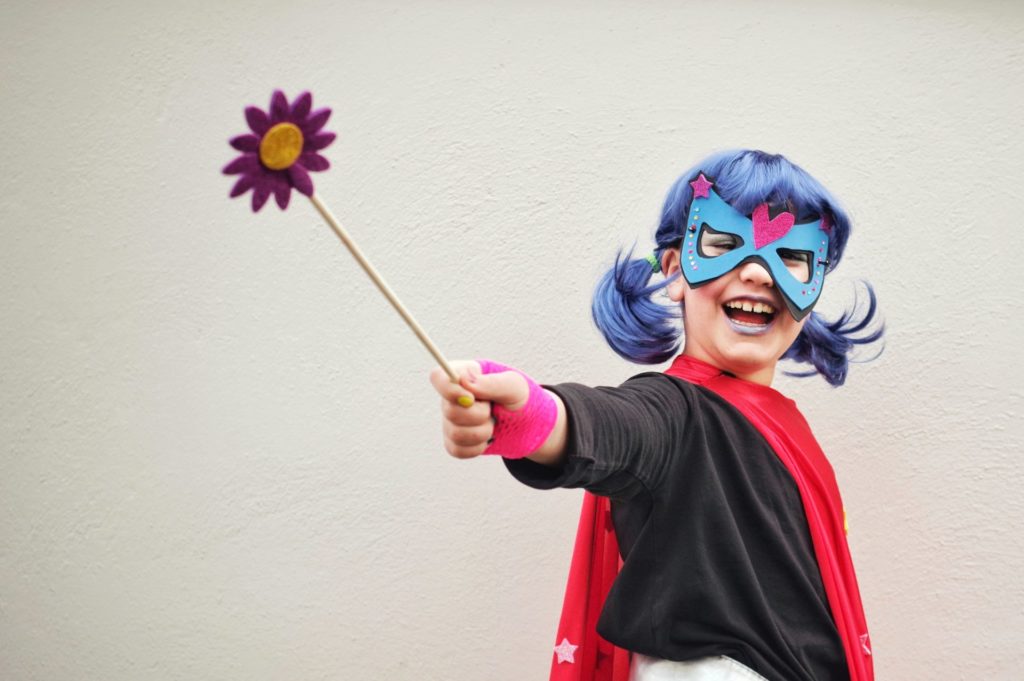 Girl with blue hair in superhero costume smiling and holding a wand